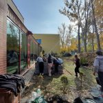 Grupa uczniów zakłada skrzyniowy ogród deszczowy: wsypują ziemię i sadzą rośliny
