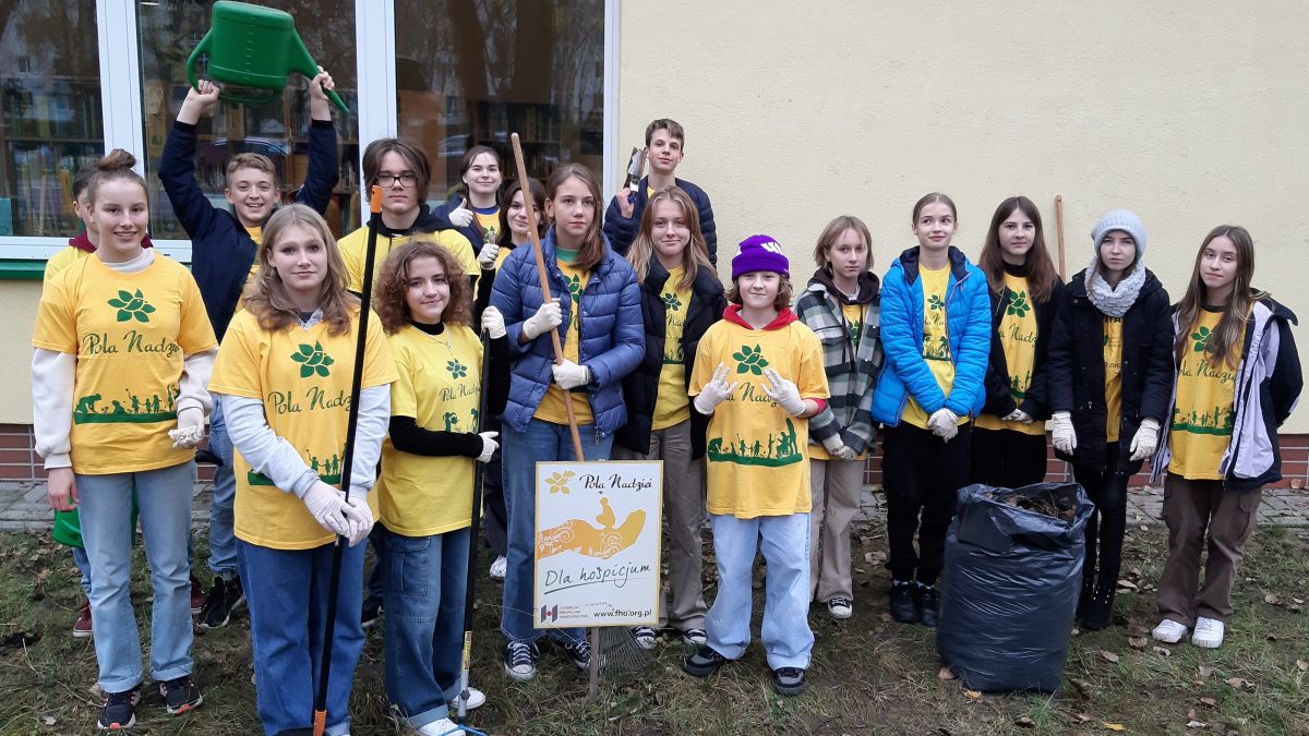 Wolontariusze z grabiami, konewką i workiem liści.