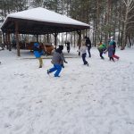 Dzieci wesoło biegają po dużym placu pokrytym śniegiem.