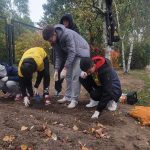 Pod budynkiem hospicjum grupa uczniów kuca i sadzi cebulki żonkili. Uczniowie są w żółtych koszulkach „Pola Nadziei”.