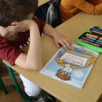 Uczniowie przy stoliku tworzą pracę na kartce