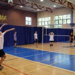 Grupa uczniów w strojach sportowych bierze udział w rozgrywkach sportowych w hali sportowej