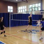 Grupa uczniów w strojach sportowych bierze udział w rozgrywkach sportowych w hali sportowej