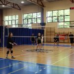 Grupa uczniów w strojach sportowych bierze udział w rozgrywkach sportowych w hali sportowej