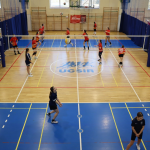 Uczniowie przebrani w stroje sportowe biorą udział w zawodach siatkówki w hali sportowej