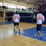 Uczniowie przebrani w stroje sportowe biorą udział w zawodach siatkówki w hali sportowej