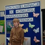 Dziecko na tle niebieskiej tablicy z napisem „szkolne eliminacje do Konkursu Warszawska Syrenka.