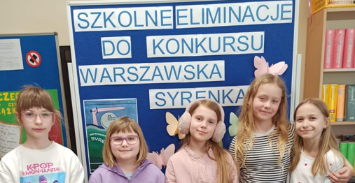 Grupa dzieci na tle niebieskiej tablicy z napisem „szkolne eliminacje do Konkursu Warszawska Syrenka.